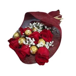 Ramo de seis rosas rojas rodeadas de pequeños puntos blancos de gypsophila, intercaladas con seis bombones dorados Ferrero Rocher, envuelto en papel decorativo elegante.