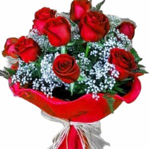 Ramo de ocho rosas rojas vibrantes rodeadas de pequeñas flores blancas de gypsophila y hojas verdes, envuelto en papel elegante con un moño de tela.