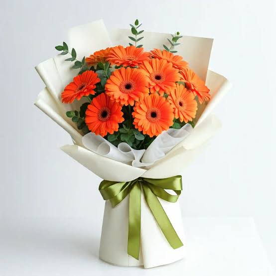 Ramo de regalo con diez gerberas de color naranja brillante rodeadas de follaje verde fresco. El ramo está envuelto de forma elegante en papel de estilo coreano y decorado con un moño de regalo en la base.